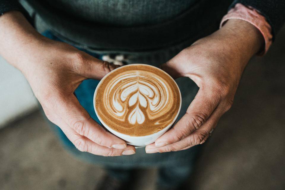 Dos manos sostienen una taza de café con arte latte