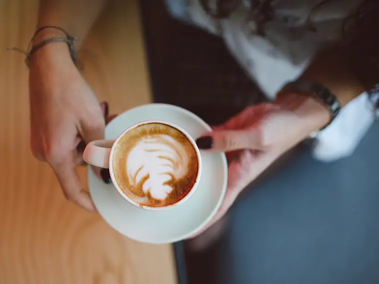 Una persona sostiene un capuchino con arte latte en una mesa de café